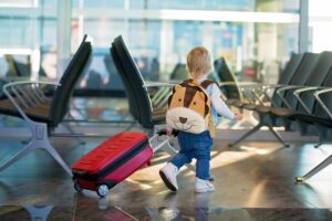 piccolo bambino in aeroporto con zainetto e valigia